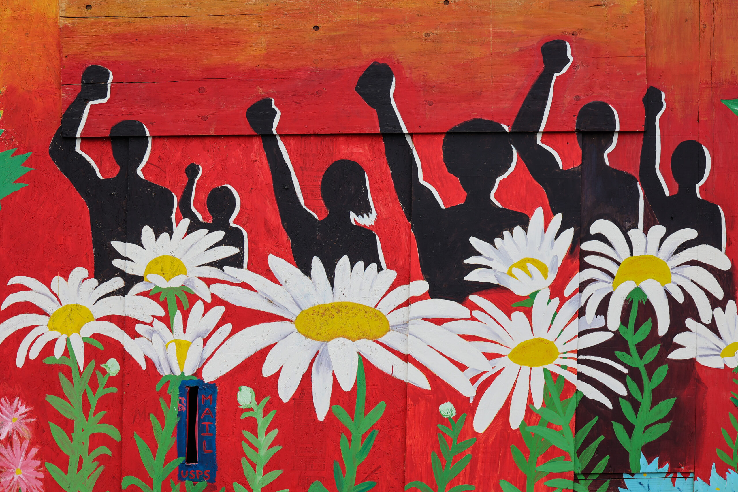 Mural of silhouetted figures raising their fists, standing behind large flowers