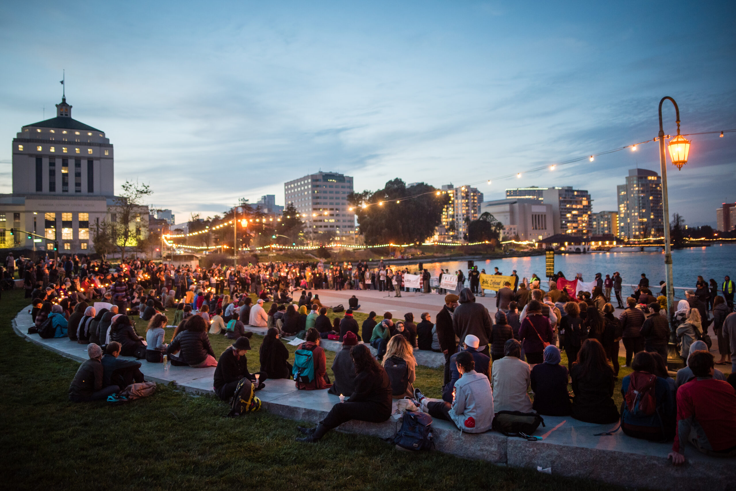 A crowd of community members gather at dusk at the edge of Lake Merritt in Oakland