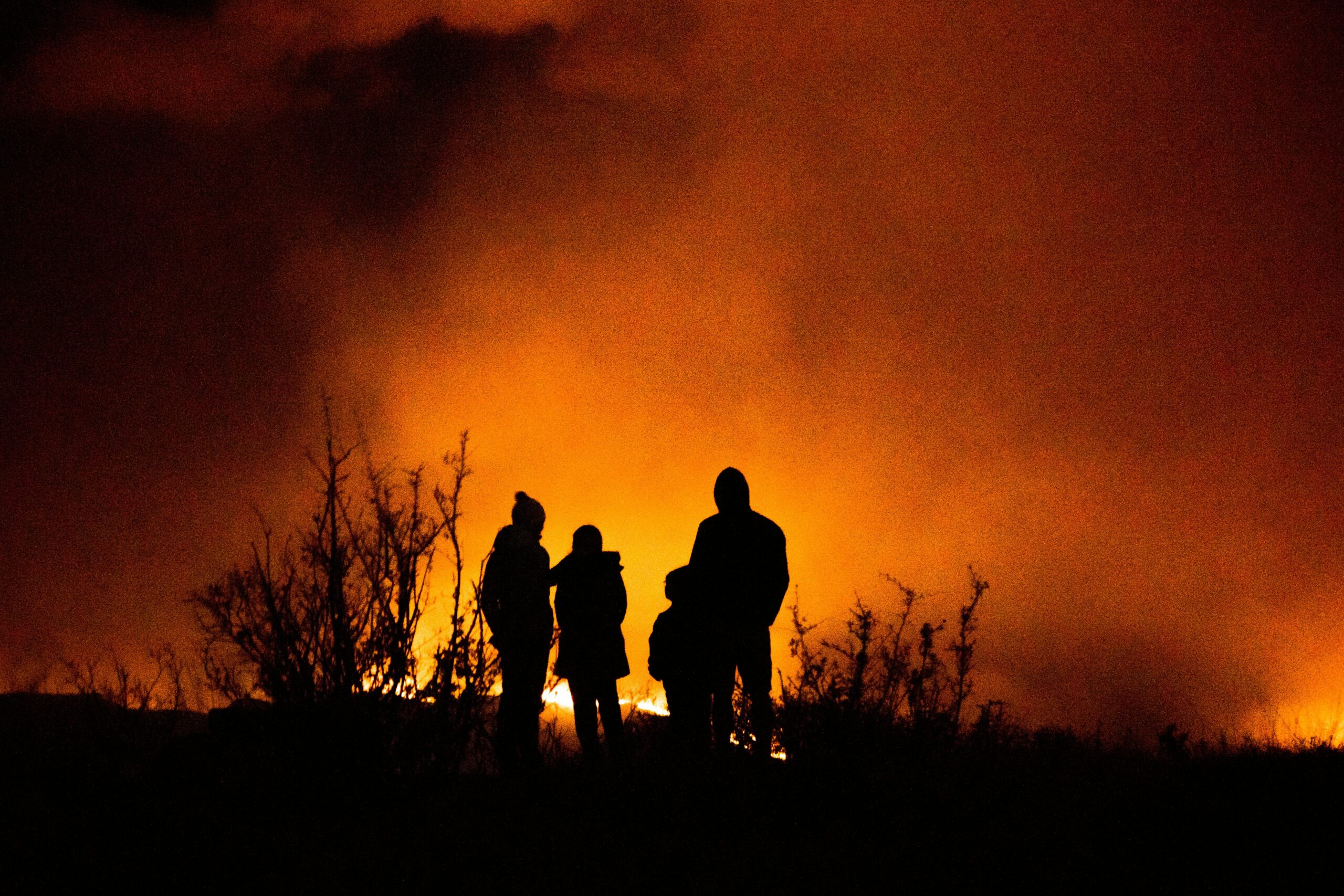 Several people stand in front of a blazing fire, glowing red against the horizon.